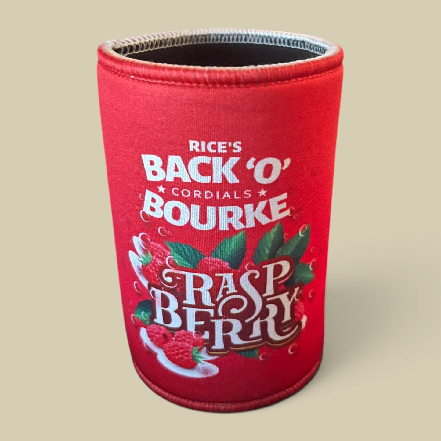 A red neoprene can cooler sleeve featuring 'Rice's Back 'O' Cordials Bourke Raspberry' branding and raspberry illustrations, shown on a solid beige background.