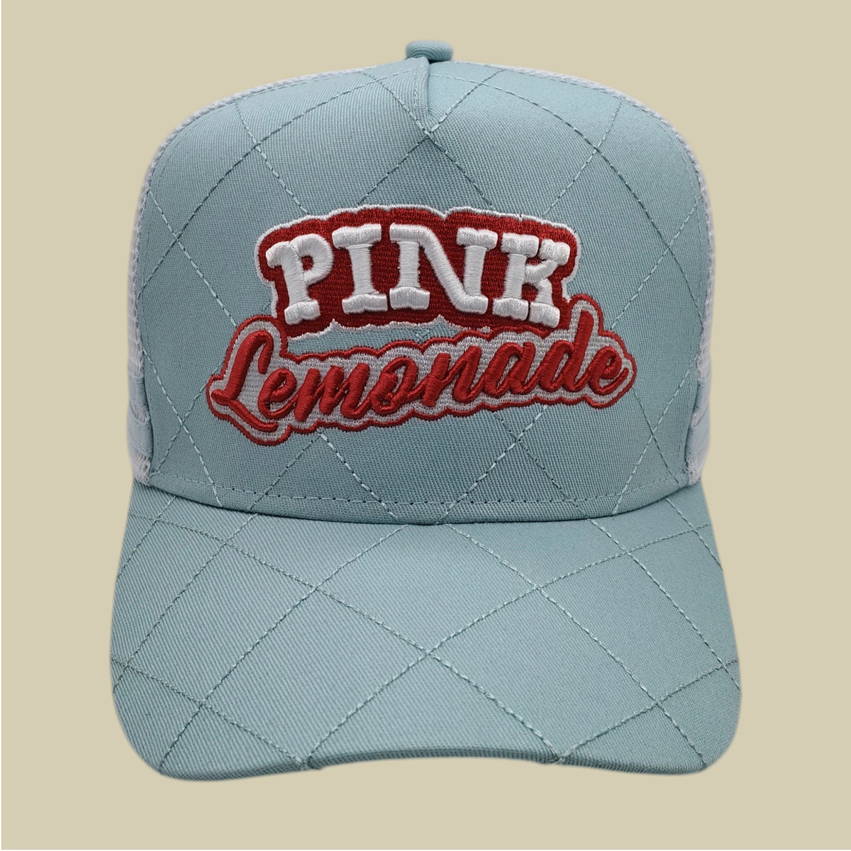 A light blue quilted trucker-style cap with 'PINK Lemonade' embroidered on the front, set against a solid beige background.