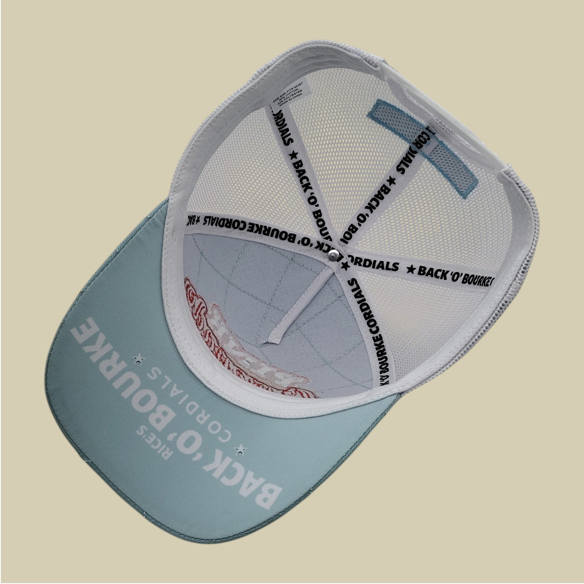 A light blue and white trucker-style cap shown from a top-down angle on a solid beige background. The brim is light blue with white text reading 'BACK O' BOURKE' and 'RIVES CORDIALS', while the mesh back is white with black text reading 'BACK O' BOURKE * RIVES CORDIALS'.