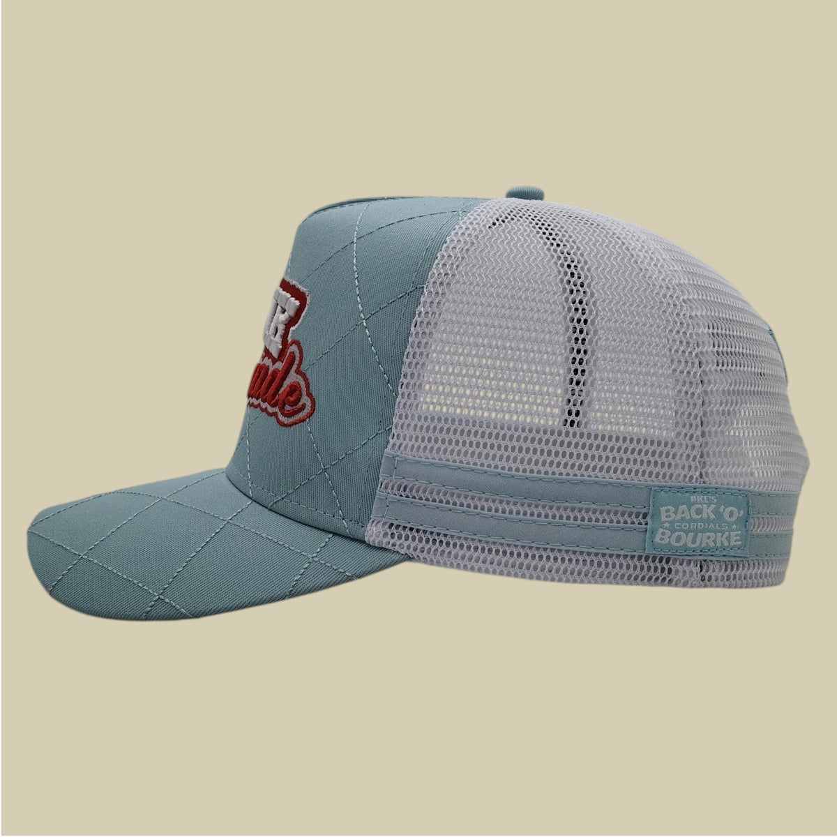 A light blue and white trucker hat with a quilted front panel, white mesh back, and red embroidered 'Raleigh' text on the side, shown against a solid beige background.