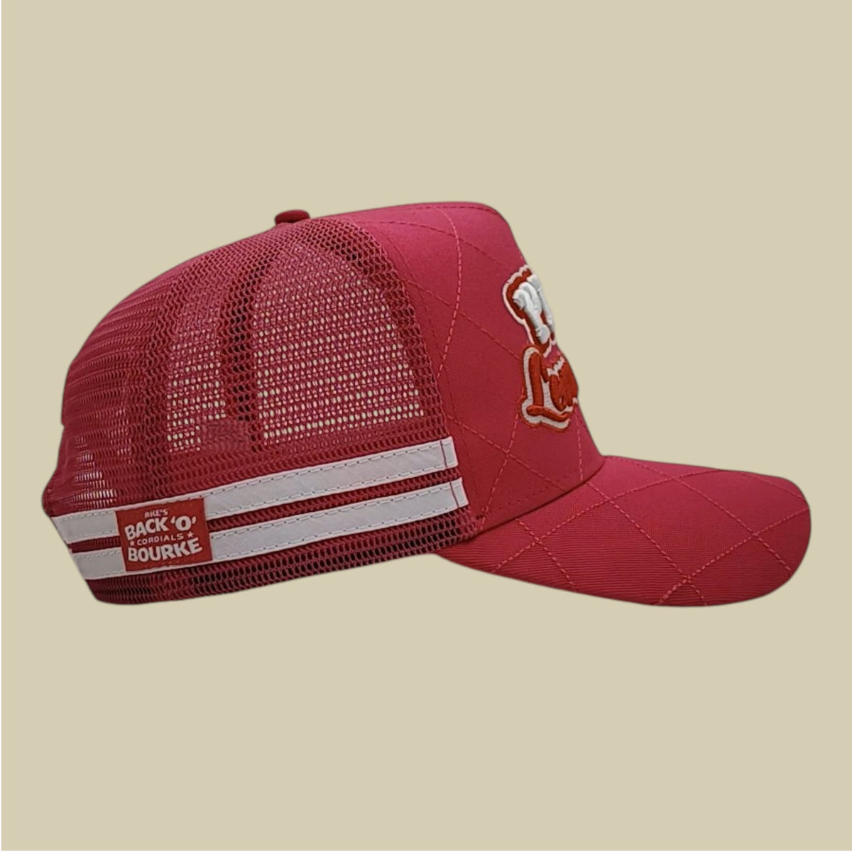 A hot pink trucker-style cap with a quilted front panel, mesh back, white horizontal stripes on the side, and a small embroidered logo on the brim, shown against a solid beige background.